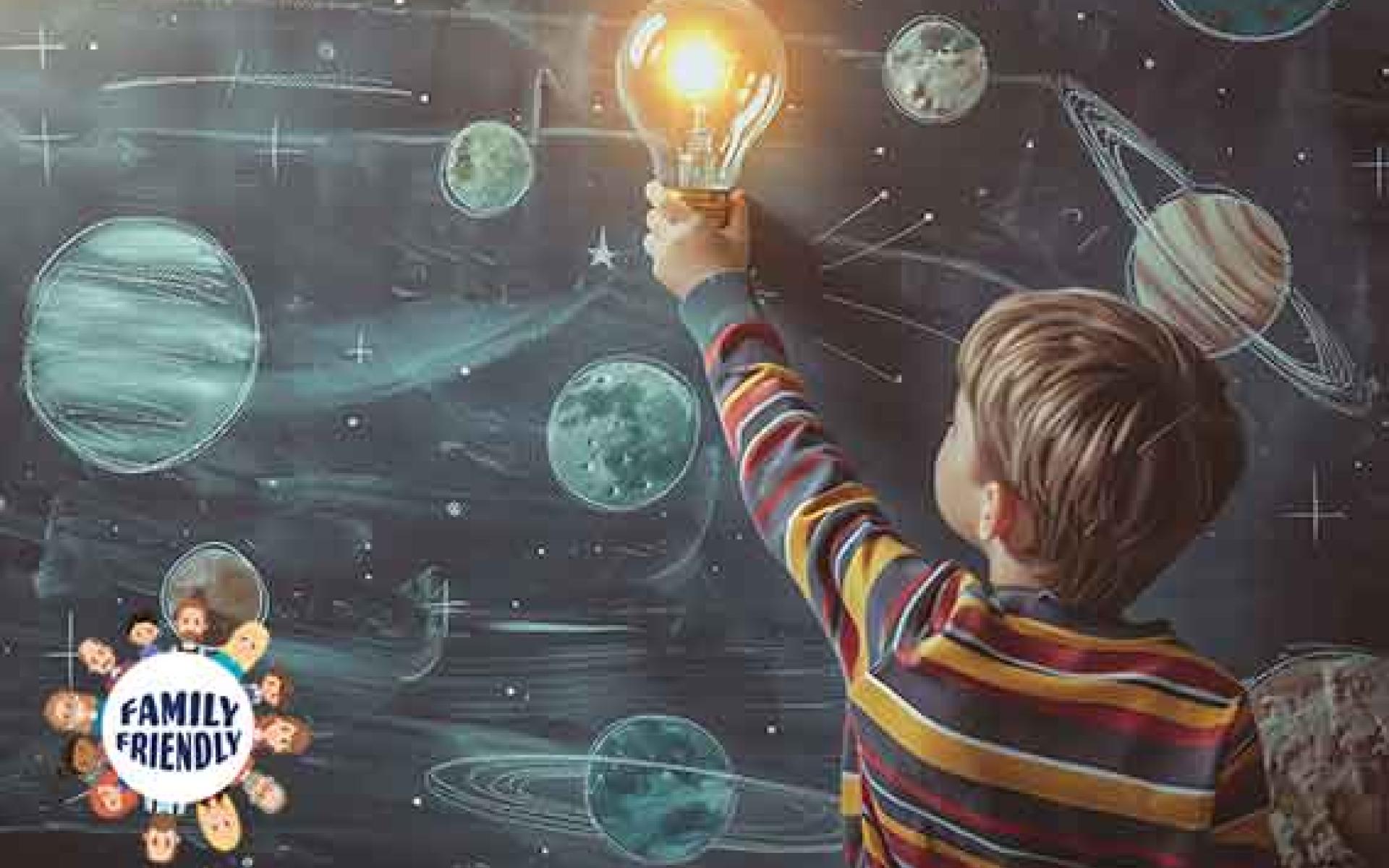Ein Junge greift nach einer Glühbirne auf einem Tafelhintergrund mit Kreidezeichnungen von Planeten und Sternen. | familyfriendly